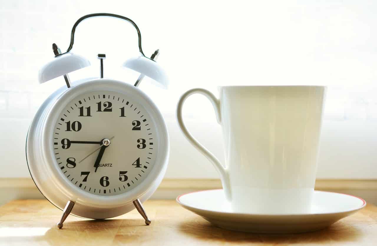 Reloj despertador junto a taza de desayuno