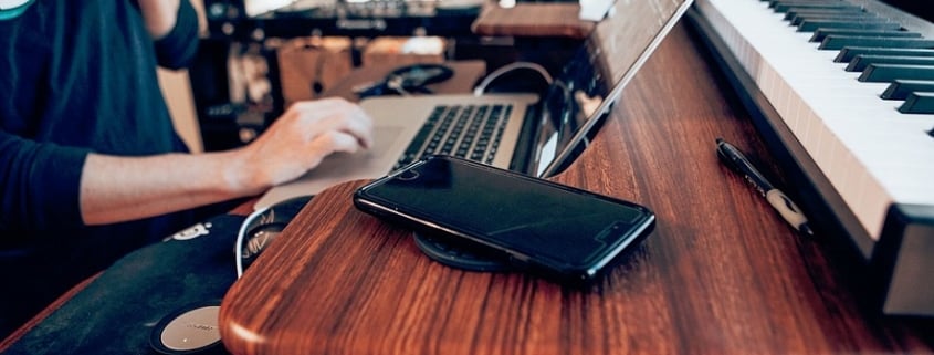 Persona utiliza un ordenador en un escritorio junto a un piano y un smartphone