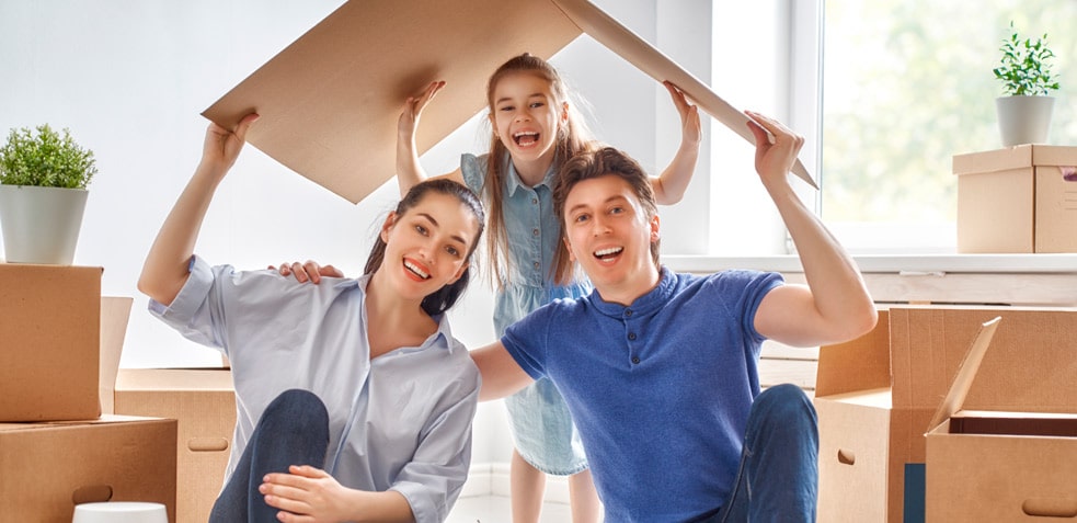 Familia feliz sostiene un cartón con forma de tejado de casa en una habitación con cajas