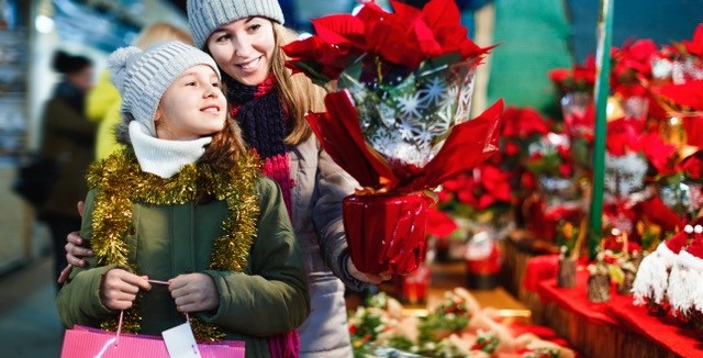 Madre e hija miran unas flores de pascua en un mercado navideño