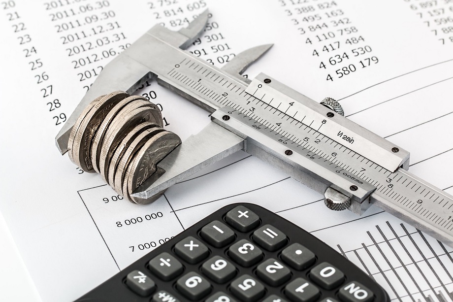 Calibre midiendo un conjunto de monedas sobre unas facturas y una calculadora