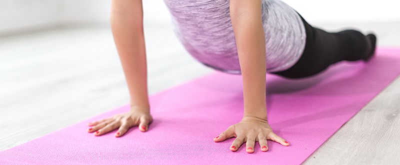 Mujer realiza ejercicios de pilates sobre una alfombra rosa