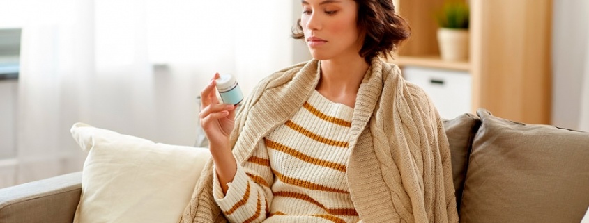 mujer sentada en un sofá mirando un bote de pastillas