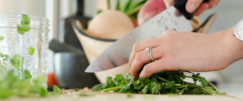 manos de una mujer con anillo cortando perejil en una cocina