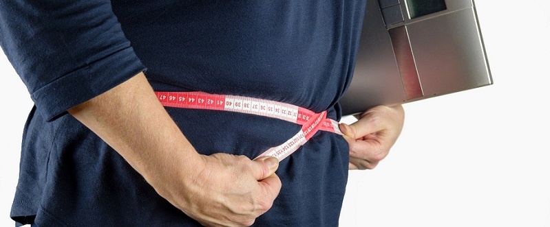 persona con una balanza y midiendo su cintura para controlar el peso