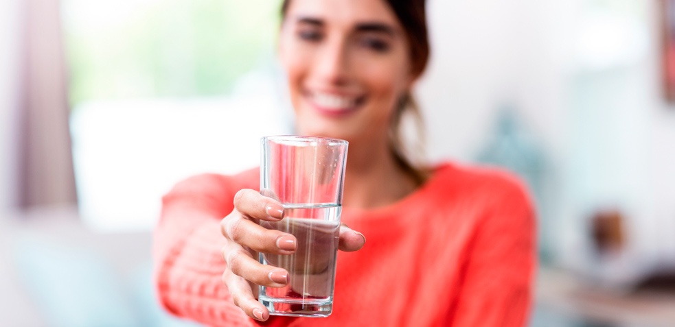 Mujer sonriente sujeta un vaso de agua 