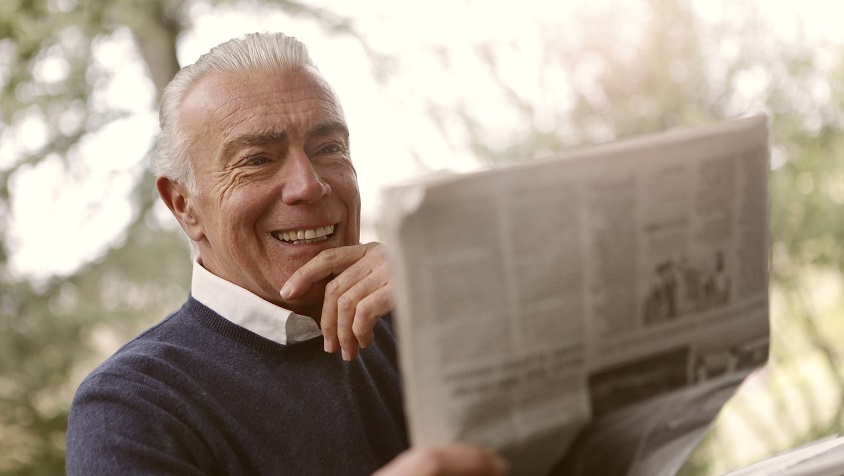 hombre jubilado y viudo leyendo el periódico felizmente en el parque