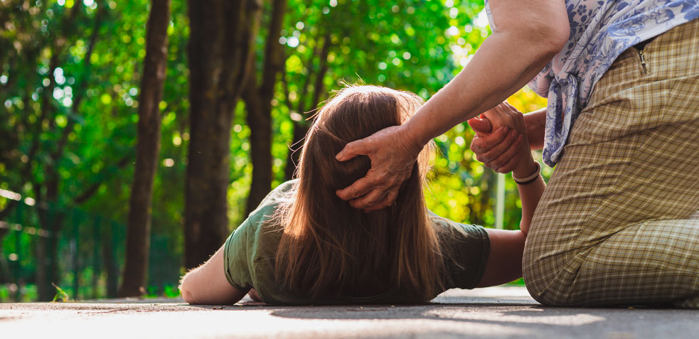 Mujer ayuda a una niña tumbada en el suelo mientras sostiene su mano y su cabeza 