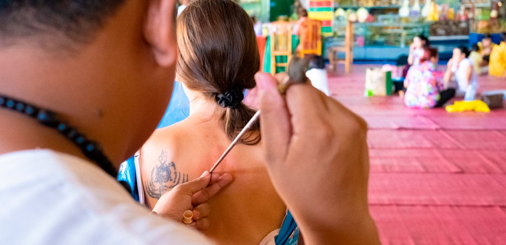 Tatuador realiza un tatuaje tradicional en la espalda de una mujer 