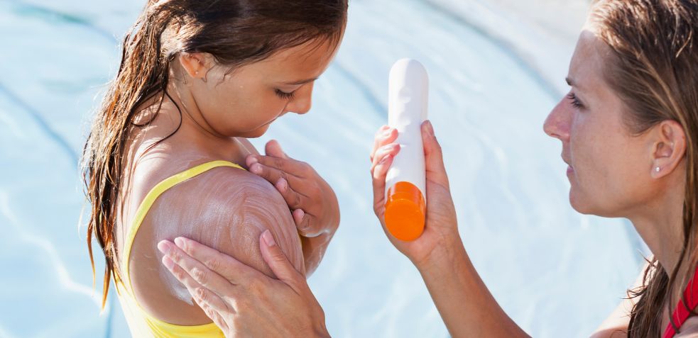 madre aplicando protector solar a su hija como forma de evitar que se queme que es uno de los riesgos en una piscina