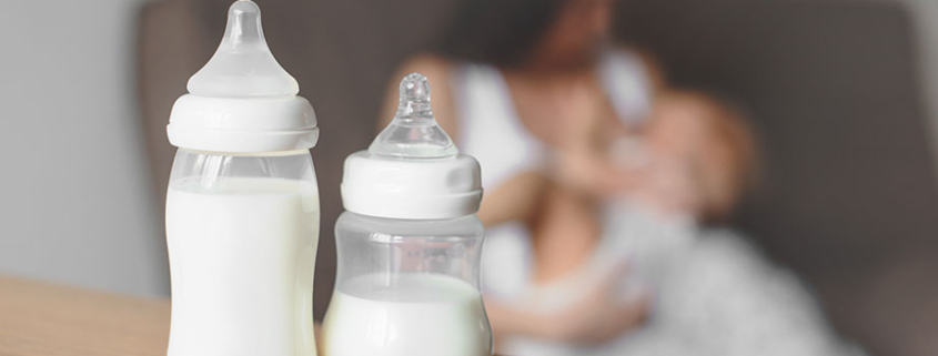 Lactancia mixta, biberones con leche de fórmula en el fondo de la madre sosteniendo en sus manos y amamantando al bebé.