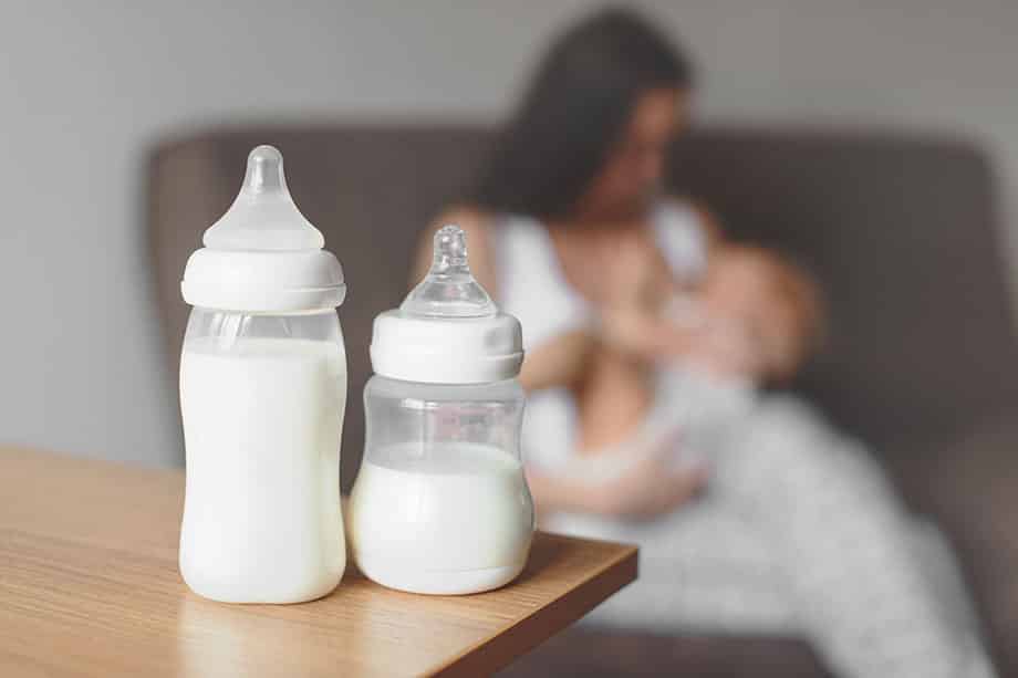 Lactancia mixta, biberones con leche de fórmula en el fondo de la madre sosteniendo en sus manos y amamantando al bebé.