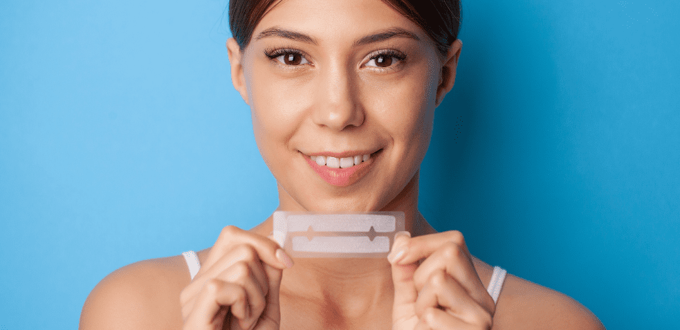 mujer mostrando tiras de blanqueamiento dental en casa