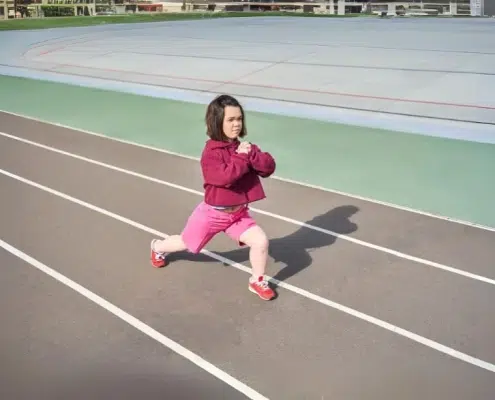 Persona con acondroplasia realizando estiramientos en una pista de atletismo