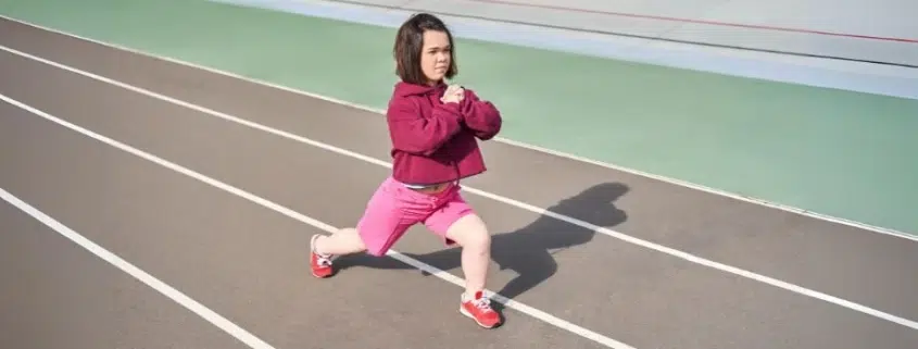 Persona con acondroplasia realizando estiramientos en una pista de atletismo