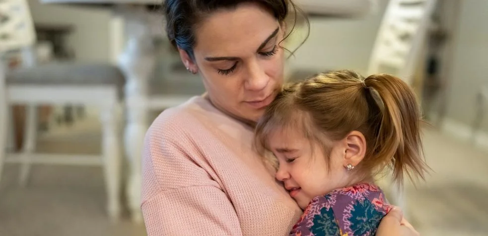 Madre consolando a su hija pequeña que llora, simbolizando el desarrollo del apego ansioso desde la infancia