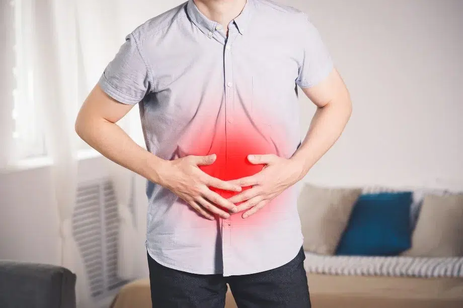 Persona con dolor abdominal agudo sosteniéndose el estómago, representando síntomas de colitis ulcerosa