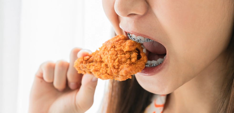 Niña con brackets comiendo pollo frito