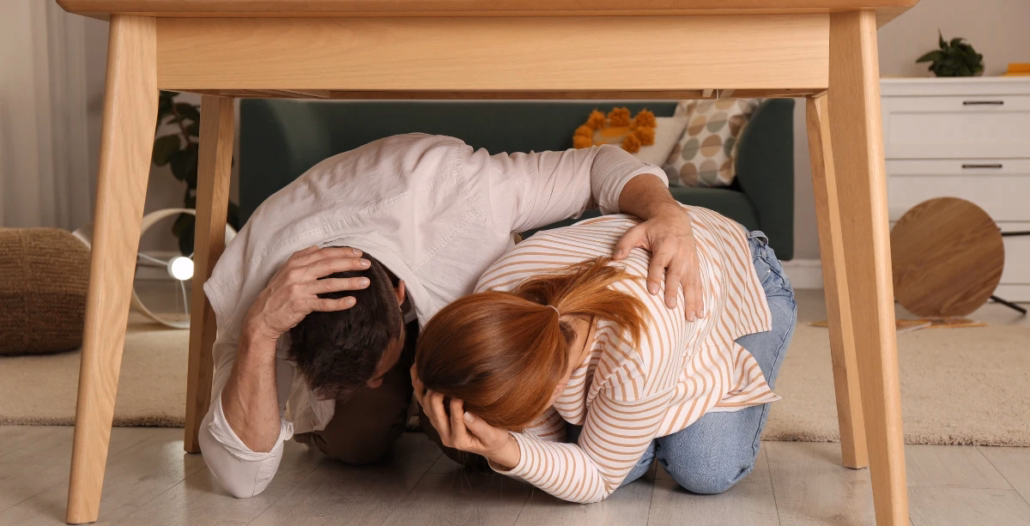 pareja protegiendose bajo una mesa durante un terremoto
