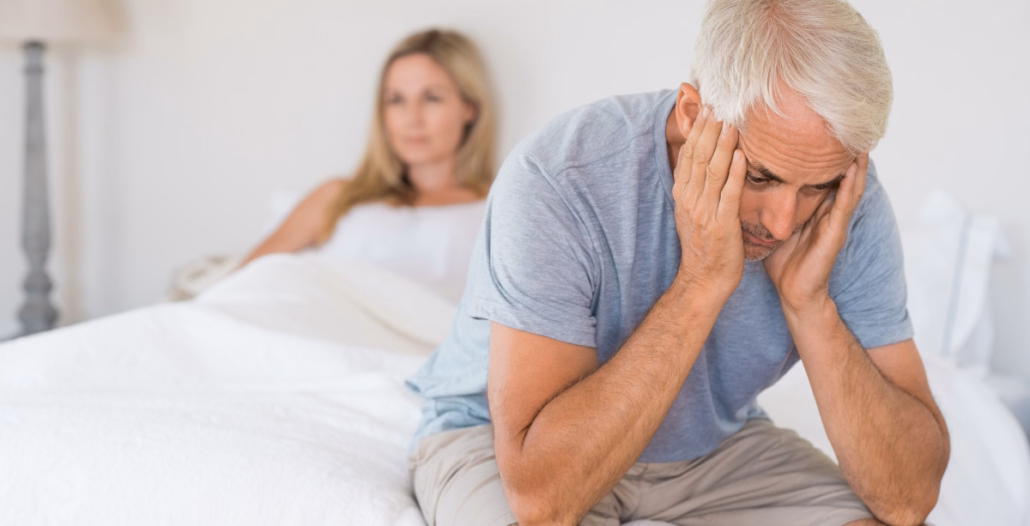 Hombre sentado en la cama con expresión de frustración, preocupado por la disfunción eréctil.